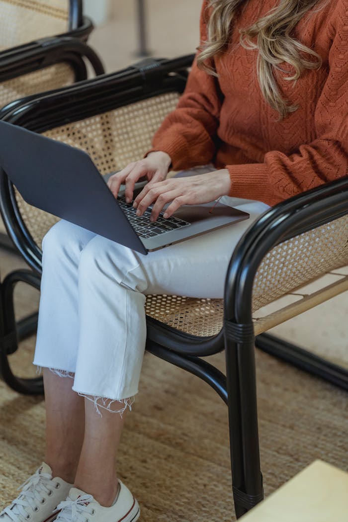 High angle of crop unrecognizable female remote employee sitting in armchair and typing on netbook while working online on startup